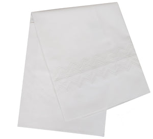 The HIVE Exclusive Arezzo Bedding Collection in white by Matouk showcases an elegantly hemstitched folded Egyptian cotton cloth with a zigzag pattern near the edge.