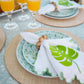 Table setting with patterned plates, a leaf-printed napkin and the Deborah Rhodes Cocoa Wood Bracelet Napkin Ring Set, plus glasses of orange juice on a light blue tablecloth and woven placemats.