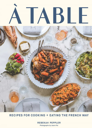The cover of "A Table" by Chronicle Books shows a marble table set with French dishes, salad, bread, and a main dish of braised meat and carrots—highlighting classic French cuisine and dining culture.