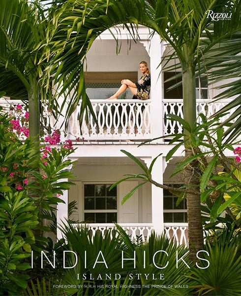 Woman sitting on a balcony surrounded by lush greenery and pink flowers with the text "India Hicks Island Style: island decorating style" below. (Rizzoli)