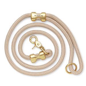 The Foggy Dog’s Marine Rope 5' Dog Leash features beige braided rope, gold hardware (clasp, ring, and bone-shaped accent), and pairs stylishly with a pink collar—perfect for chic walks or outings to the dog park.