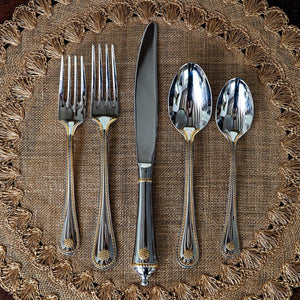 Sentence with replaced product: Juliska Silverware set including two forks, a knife, and two spoons arranged neatly on a textured woven mat in the style of French tradition flatware.