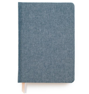 The Sugar Paper Tailored Journal in Chambray features a closed blue fabric cover, lined pages, and a beige ribbon bookmark against a white background.