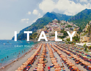 A lively beach with orange umbrellas and a colorful hillside town captures iconic Italian coast charm. "Gray Malin: Italy" by Pink Chicken is perfect for anyone who loves Italy and stunning coastal photography.