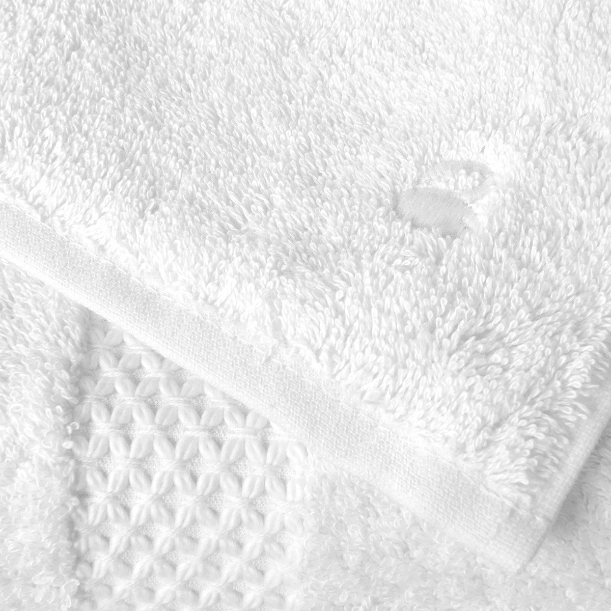 Close-up of an Etoile Blanc Bath Towel from Yves Delorme, featuring textured patterns in a luxurious cotton blend fabric and a small hole near the edge.