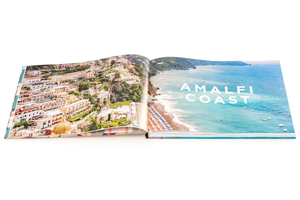 An open book from Pink Chicken's "Gray Malin: Italy" reveals an aerial photo of the Italian coast with buildings, shoreline, and boats, featuring "AMALFI COAST" on the right page—a striking highlight in this Italy photography book.