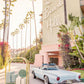 Gray Malin’s "Joy Ride, The Beverly Hills Hotel" (15.5” x 21”, White Frame) features a pale blue vintage convertible and gold luggage cart under palm trees, capturing retro glamour in Gray Malin's iconic style.
