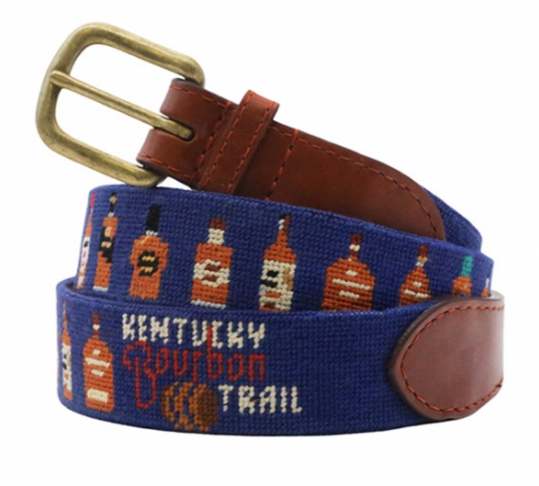 The Smathers & Branson Kentucky Bourbon Trail Bottles Belt by Smathers & Branson is a blue needlepoint belt with brown vegetable tanned Italian leather accents, displaying an embroidered pattern of bourbon bottles and the text "Kentucky Bourbon Trail," featuring a solid brass buckle.