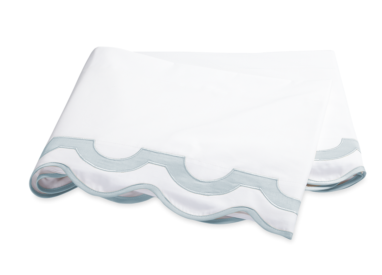 A folded white sheet with a scalloped edge in pool blue, crafted from luxurious Egyptian cotton percale, exemplifies the signature softness and elegance of the Matouk Mirasol Bedding Collection.