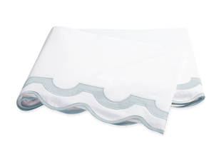 A folded white sheet with a scalloped edge in pool blue, crafted from luxurious Egyptian cotton percale, exemplifies the signature softness and elegance of the Matouk Mirasol Bedding Collection.