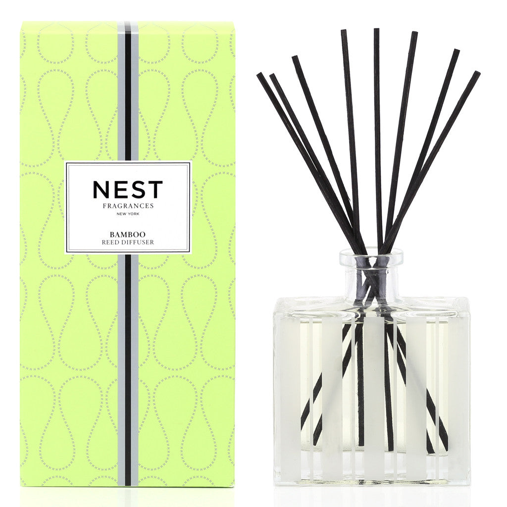 A green box labeled "Nest Bamboo Diffuser" sits beside a clear glass jar with black reeds, ideal for filling your space with lush bamboo scents using Nest’s premium fragrance oils.