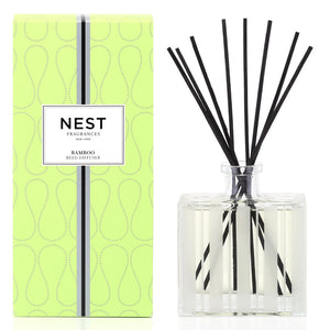 A green box labeled "Nest Bamboo Diffuser" sits beside a clear glass jar with black reeds, ideal for filling your space with lush bamboo scents using Nest’s premium fragrance oils.