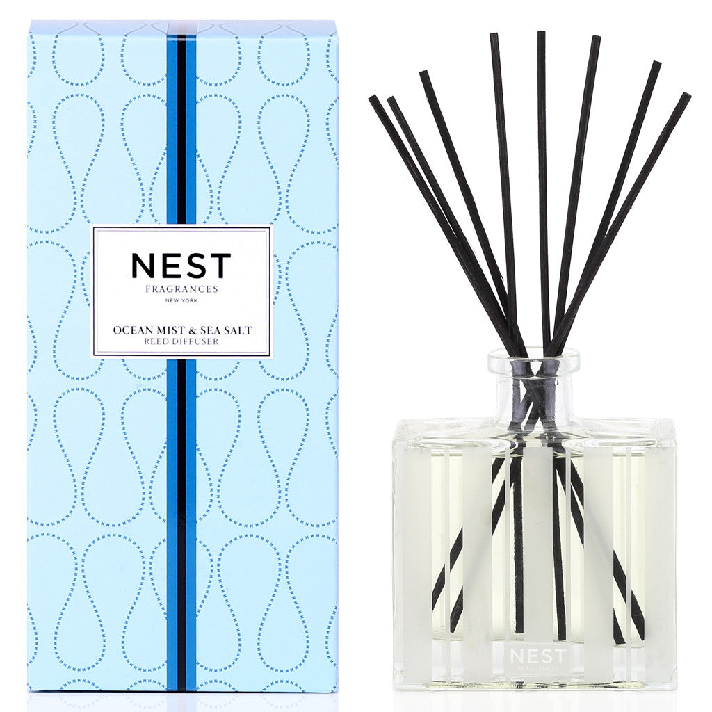A Nest Ocean Mist & Sea Salt Reed Diffuser sits beside a clear glass bottle with black reeds, offering a refreshing ocean-inspired scent for your home.