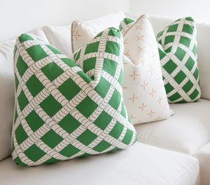 A white sofa is adorned with four throw pillows. Two feature a green and white lattice pattern, while the other two have a white background with small orange crosses—each one a handmade, down-filled Petite Cross and Dot Peach Pillow crafted in the USA by Edgar Custom Drapery.
