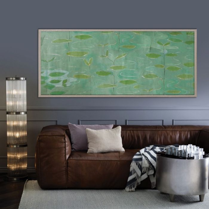 A living room with a brown leather sofa, cushions, striped throw, metallic side table, tall lamp, a large green abstract painting, and Lilies by Paule Marrot in Acrylic Box from Natural Curiosities on the wall.