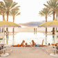 Relax by the pool under yellow umbrellas and palm trees with Gray Malin Poolside The Breakers Palm Beach, White Frame, 29.5" x 41.5", capturing an ocean view at sunset and a stylish scene of friends playing backgammon poolside.