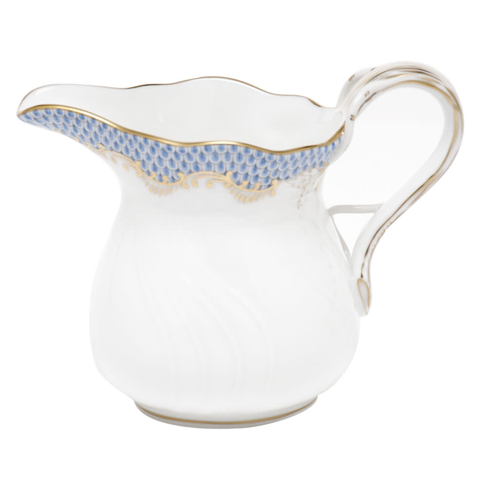 A light blue porcelain pitcher with a curvy handle, featuring blue and gold fish scale decorative patterns near the rim, and a scalloped edge. The design exudes elegance reminiscent of Herend craftsmanship.