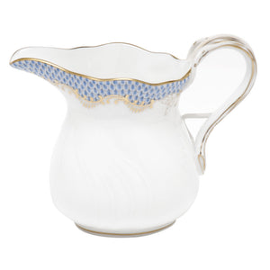 A light blue porcelain pitcher with a curvy handle, featuring blue and gold fish scale decorative patterns near the rim, and a scalloped edge. The design exudes elegance reminiscent of Herend craftsmanship.