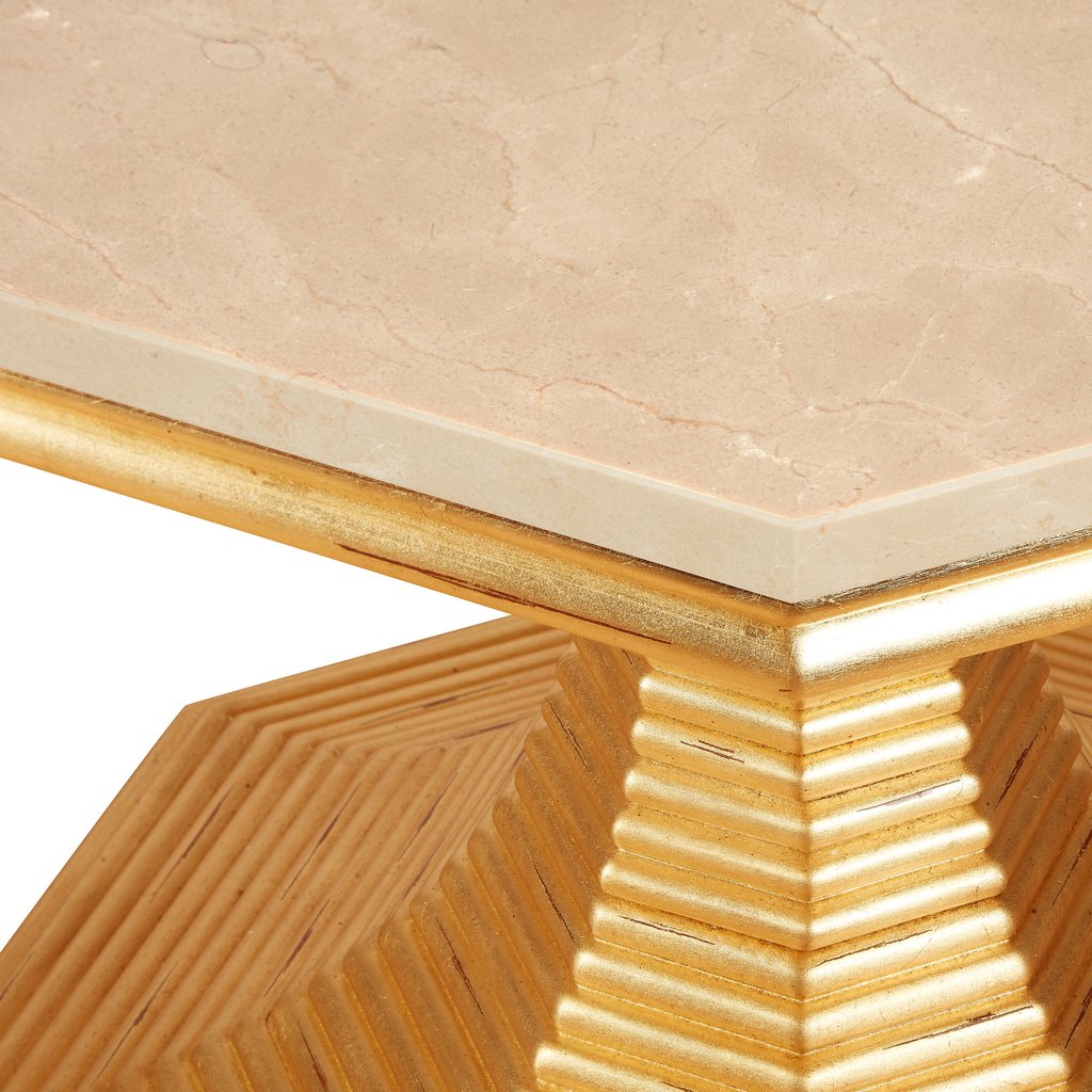 A close-up of the Hourglass Table by Bunny Williams reveals a marble tabletop corner with an antique gold-edged base featuring stepped, geometric ridges.