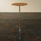 The Ruislip Side Table by Mr Brown stands elegantly on a dark, textured surface with its slender profile, round top, and three curved legs. Its Verona Gold finish shimmers subtly in the light.
