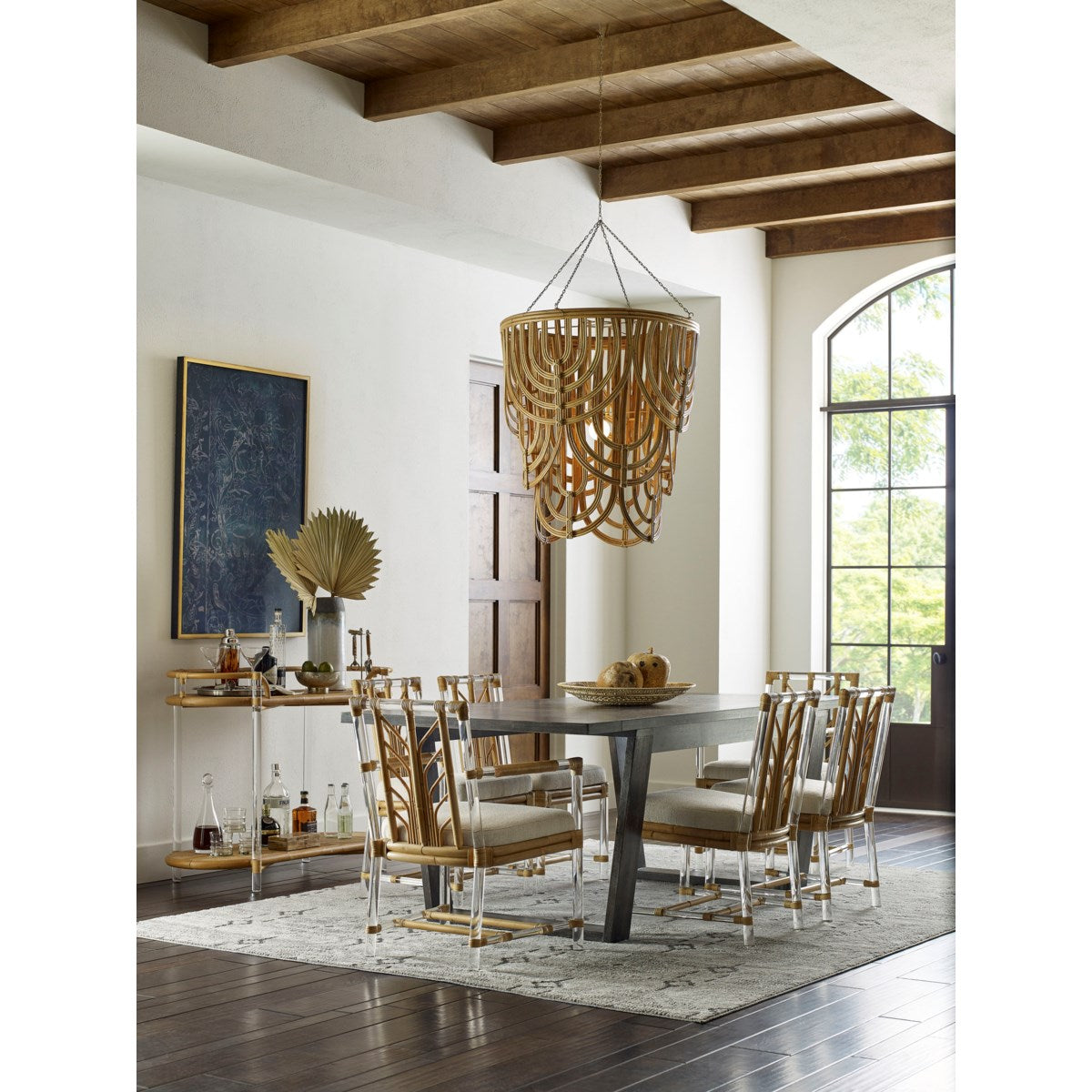 The dining room boasts a large wooden table with eight chairs, a decorative chandelier, and Selamat's Acrylic and Rattan Console. Inlaid details enhance the bar cart, while ceiling beams and an arched window reflect Sea Cliff's charm.