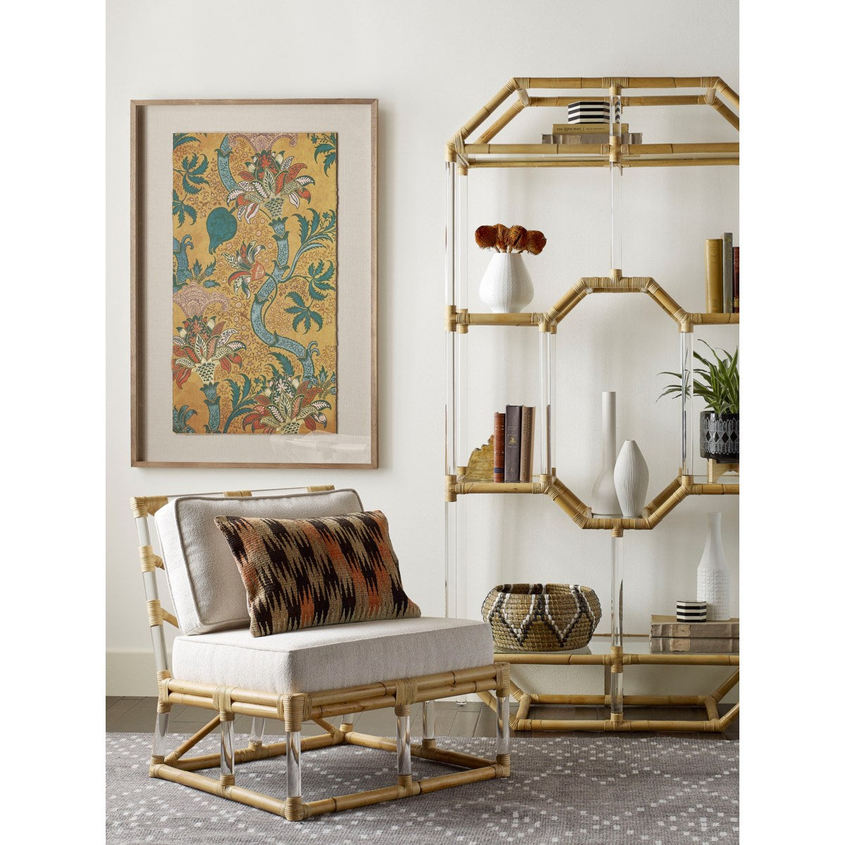 A room corner featuring the Sea Cliff Slipper Chair by Selamat, elegantly upholstered in Kravet Crypton Boucle Fabric, accompanied by a patterned throw pillow. The space is complemented by a rattan hand-bent shelving unit displaying decor items and framed floral artwork on the wall, all inspired by the serene beauty of Sea Cliff.