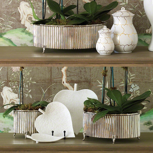 Two shelves display Global Views Small Nickel Corrugated Bamboo Cachepots with green plants, white ceramic jars with gold lines, and white leaf-shaped plates, all set against decorative nature-inspired wallpaper.