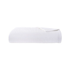 The Songe Blanc Quilted Coverlet by Yves Delorme is a white textured cotton blanket with a subtle chevron pattern, shown folded against a plain white background.