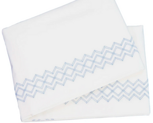 A pair of luxurious white bedsheets from the HIVE Exclusive Arezzo Bedding Collection by Matouk features cloud blue zigzag patterns along the edges, crafted from Egyptian cotton.