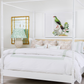 A white four-poster bed features Sorella Glenn’s Feather Ikat Shade in Spearmint bedding in a bright bedroom, paired with a green lamp. Above the bed are a gold-framed mirror and bird artwork.