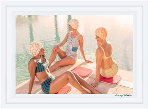 Three individuals in retro swimwear and floral caps relax on red mats poolside, evoking Palm Beach style and the timeless elegance of Gray Malin's "Bathing Beauties" print, 29.5" x 41.5", White Frame.