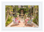 A group in colorful attire gathers by a central fountain in a lush courtyard at The Breakers hotel, surrounded by palm trees and greenery, capturing the vibrant essence of the Gray Malin Palm Courtyard at The Breakers Palm Beach, with a white frame measuring 29.5" x 41.5".