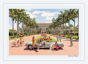 In Gray Malin's The Breakers Palm Beach, vibrant people surround a vintage convertible with a dog against a palm-lined, luxurious building backdrop.