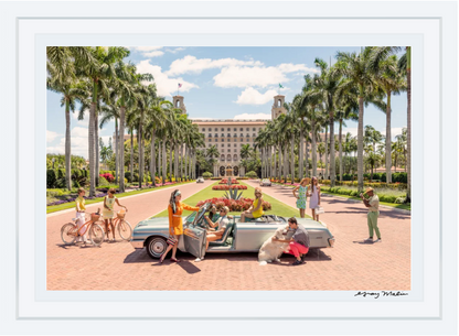 In Gray Malin's The Breakers Palm Beach, vibrant people surround a vintage convertible with a dog against a palm-lined, luxurious building backdrop.